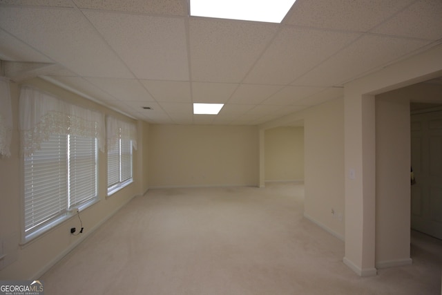 spare room featuring baseboards, a drop ceiling, and light colored carpet