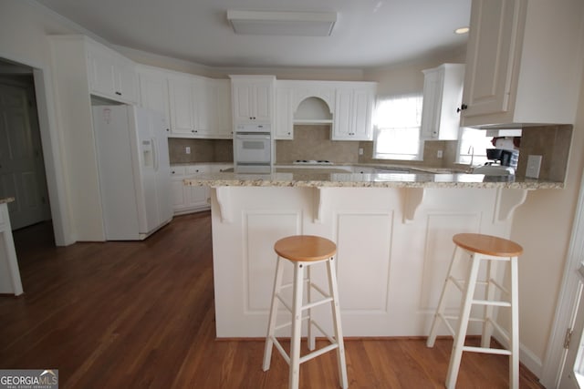 kitchen featuring dark wood-style floors, white appliances, a peninsula, and decorative backsplash