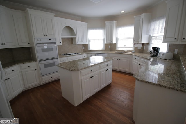 kitchen with white appliances, white cabinetry, dark wood-style flooring, and a center island