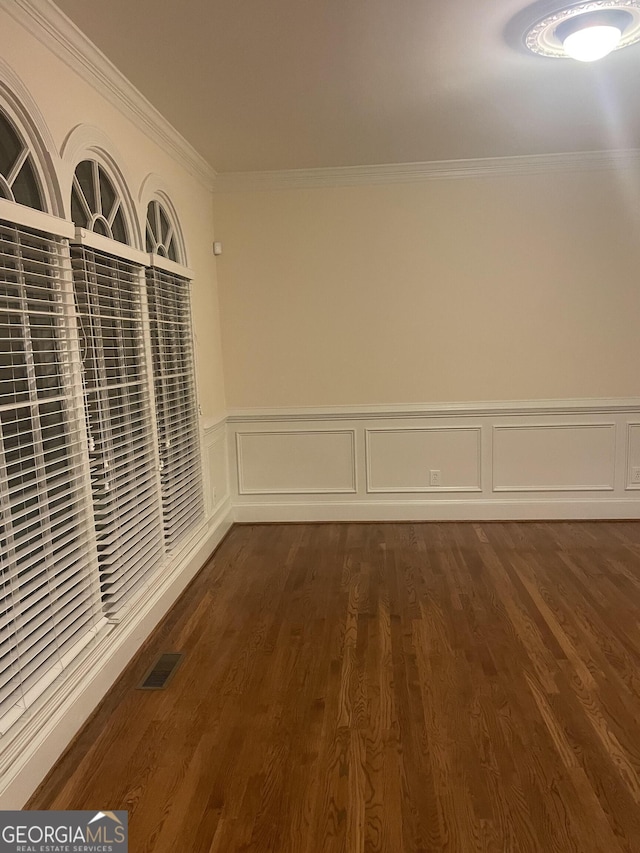 unfurnished room with ornamental molding, dark wood-type flooring, a wainscoted wall, and visible vents