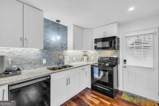 kitchen with white cabinets, dark wood-style floors, light stone counters, black appliances, and a sink