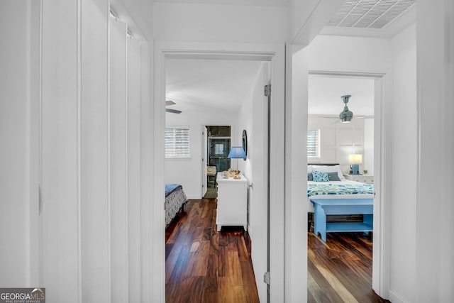 hallway with dark wood-type flooring, visible vents, and baseboards