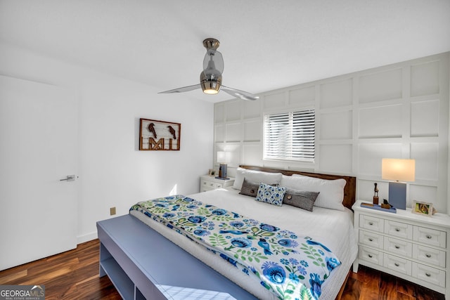 bedroom with a ceiling fan, a decorative wall, and dark wood-type flooring