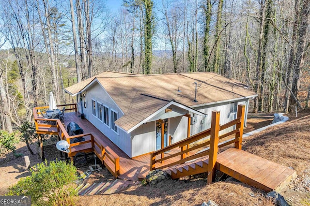 view of front of property with a forest view, a shingled roof, and a wooden deck