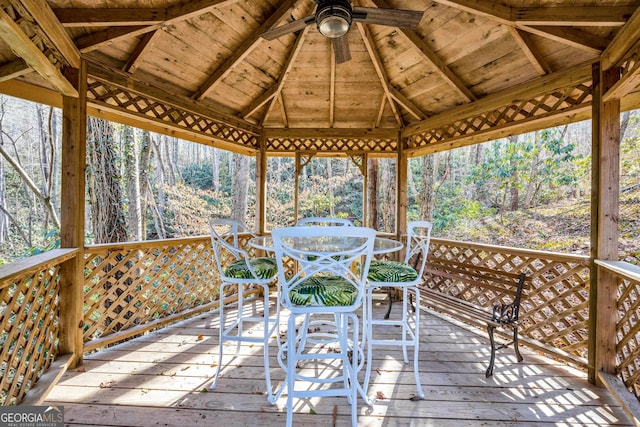 wooden terrace with a gazebo, outdoor dining space, and a view of trees