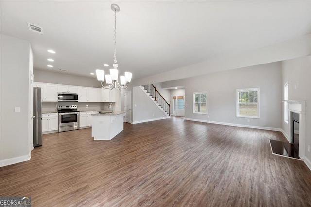 unfurnished living room with dark wood finished floors, a notable chandelier, visible vents, a fireplace with flush hearth, and baseboards