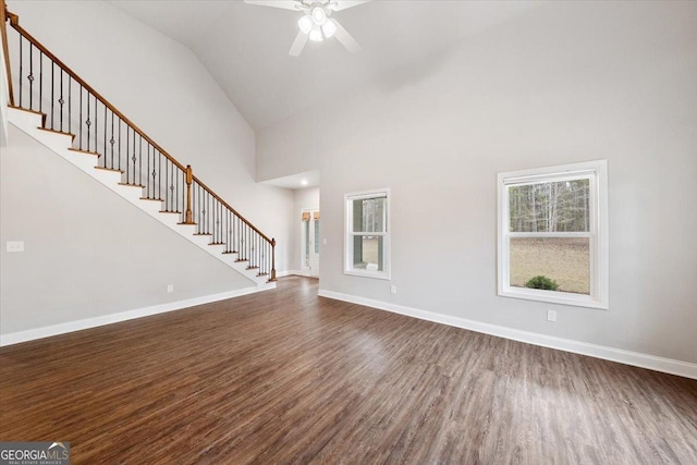 unfurnished living room with high vaulted ceiling, dark wood-style flooring, stairway, and baseboards