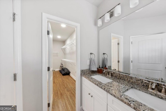 full bath featuring double vanity, wood finished floors, a spacious closet, and a sink