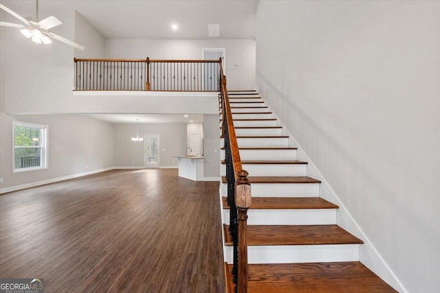 stairs featuring ceiling fan, a towering ceiling, baseboards, and wood finished floors