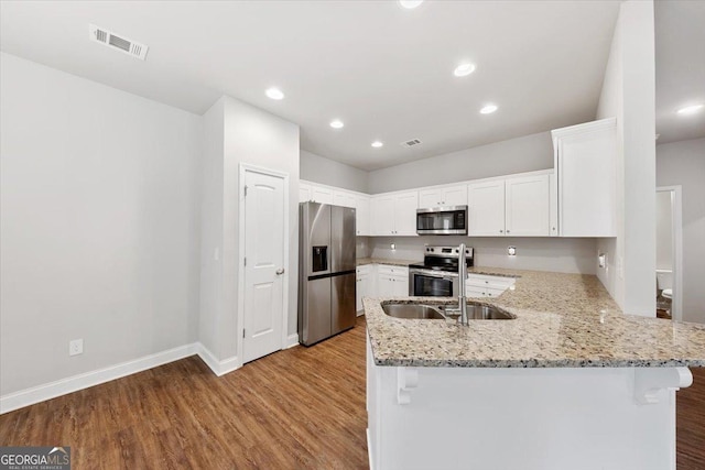 kitchen with stainless steel appliances, a peninsula, visible vents, light stone countertops, and light wood finished floors