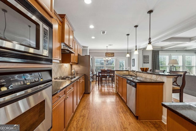 kitchen with light wood-style flooring, under cabinet range hood, a sink, appliances with stainless steel finishes, and brown cabinetry