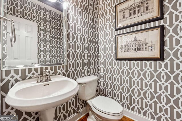 half bath featuring baseboards, a sink, toilet, and wallpapered walls