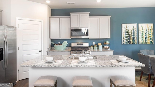 kitchen with light stone counters, visible vents, appliances with stainless steel finishes, an island with sink, and a kitchen bar