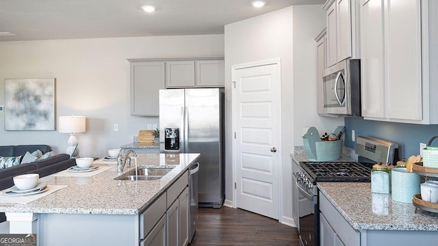 kitchen with light stone counters, dark wood-type flooring, a sink, appliances with stainless steel finishes, and gray cabinets