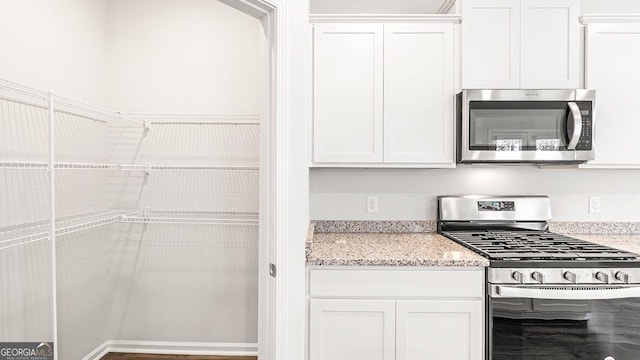 kitchen featuring appliances with stainless steel finishes, white cabinets, and light stone counters