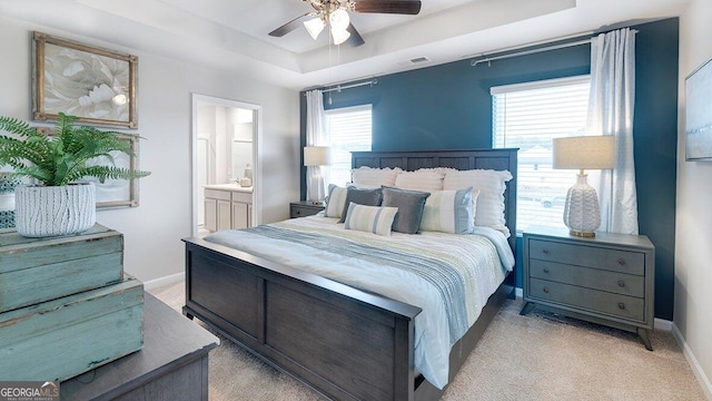 bedroom with light carpet, baseboards, visible vents, ensuite bath, and a tray ceiling