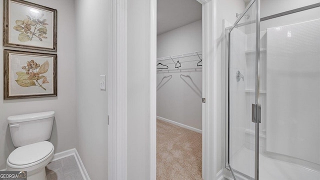 full bath featuring toilet, a shower stall, baseboards, and a walk in closet