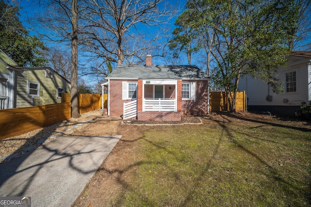 view of front facade featuring brick siding, a chimney, a front yard, and fence