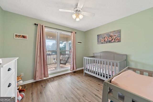 bedroom featuring a ceiling fan, a crib, baseboards, and wood finished floors