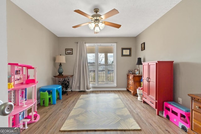 game room with a textured ceiling, baseboards, a ceiling fan, and light wood-style floors