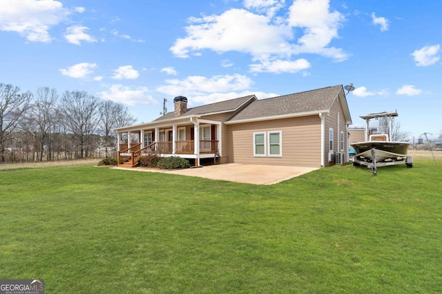 back of property featuring covered porch, a chimney, a lawn, and a patio