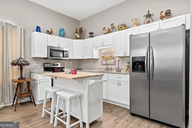 kitchen featuring stainless steel appliances, a sink, wood counters, light wood-style floors, and white cabinets