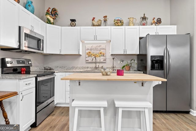 kitchen with a center island, stainless steel appliances, wooden counters, white cabinetry, and a sink