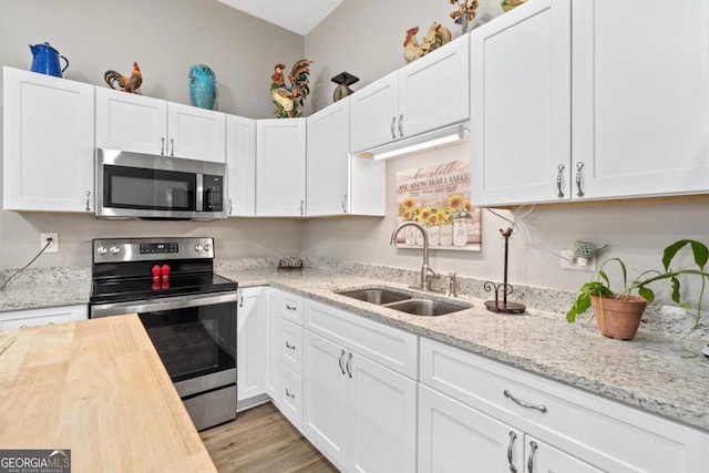 kitchen featuring white cabinets, butcher block counters, light wood-style flooring, appliances with stainless steel finishes, and a sink