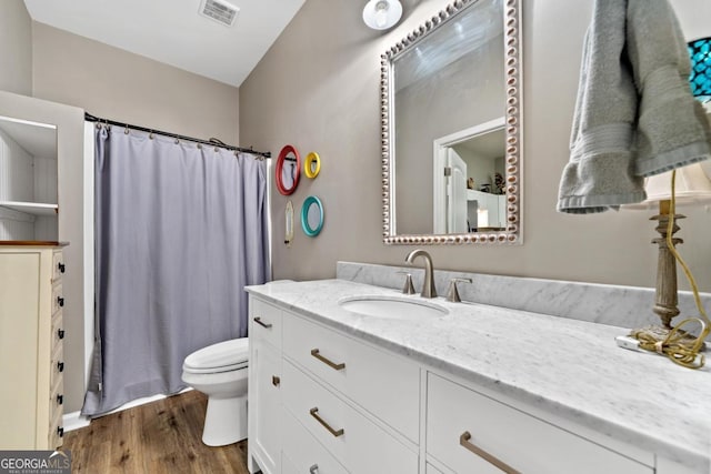 full bath with toilet, a shower with shower curtain, wood finished floors, vanity, and visible vents