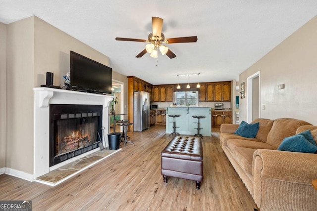 living area featuring light wood-style floors, a lit fireplace, and a ceiling fan