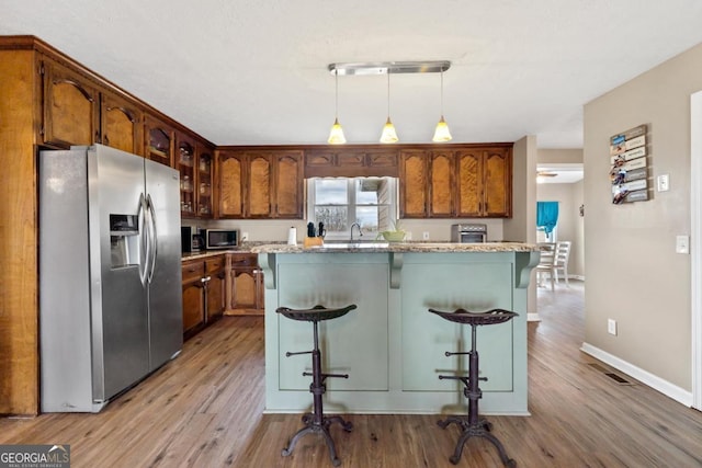 kitchen with stainless steel appliances, hanging light fixtures, a breakfast bar area, and wood finished floors