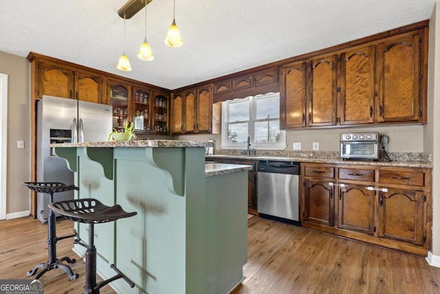 kitchen featuring light wood-style flooring, a kitchen island, appliances with stainless steel finishes, a kitchen bar, and pendant lighting