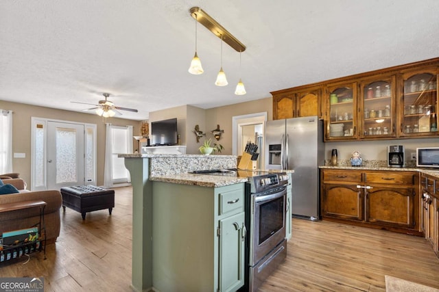 kitchen featuring a kitchen island, open floor plan, appliances with stainless steel finishes, light wood finished floors, and glass insert cabinets