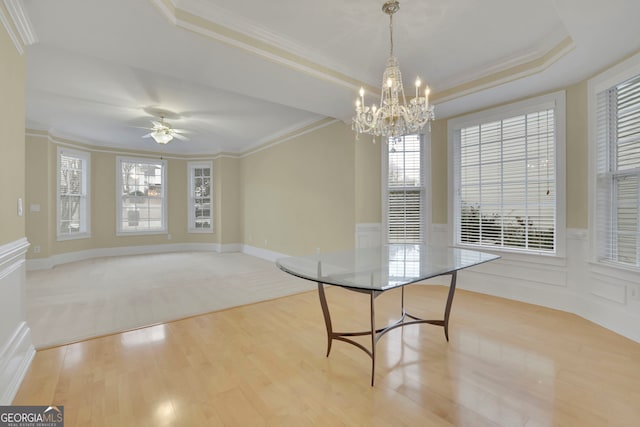 unfurnished dining area with a tray ceiling, wainscoting, light wood finished floors, and ornamental molding