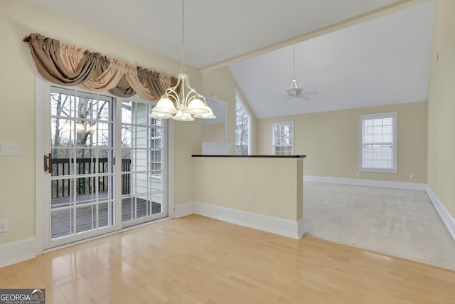 unfurnished dining area with ceiling fan with notable chandelier, vaulted ceiling, wood finished floors, and baseboards