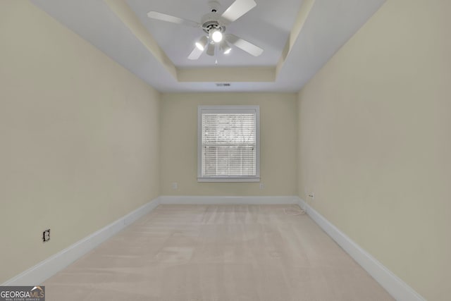 spare room with visible vents, baseboards, ceiling fan, light colored carpet, and a tray ceiling