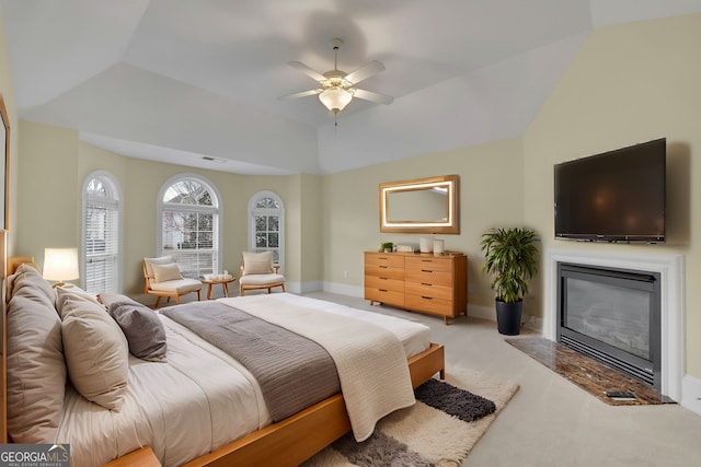 bedroom featuring a glass covered fireplace, lofted ceiling, a ceiling fan, and light carpet