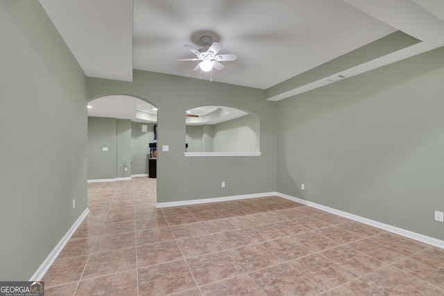 tiled spare room with arched walkways, visible vents, a ceiling fan, and baseboards