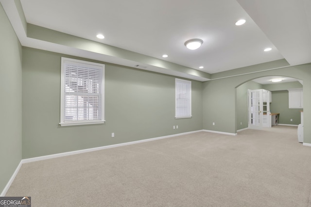 empty room featuring recessed lighting, baseboards, arched walkways, and light carpet