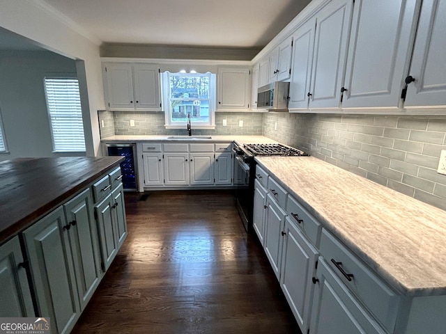 kitchen with beverage cooler, appliances with stainless steel finishes, a sink, and white cabinetry