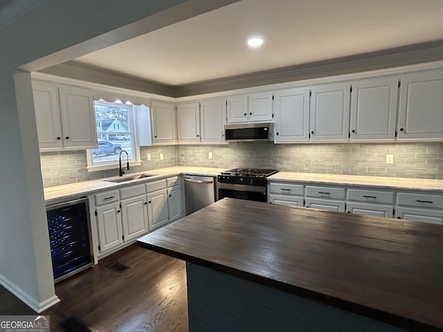 kitchen with beverage cooler, dark wood finished floors, appliances with stainless steel finishes, wooden counters, and a sink