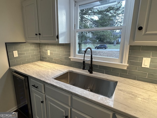 kitchen with light stone counters, tasteful backsplash, white cabinets, a sink, and beverage cooler