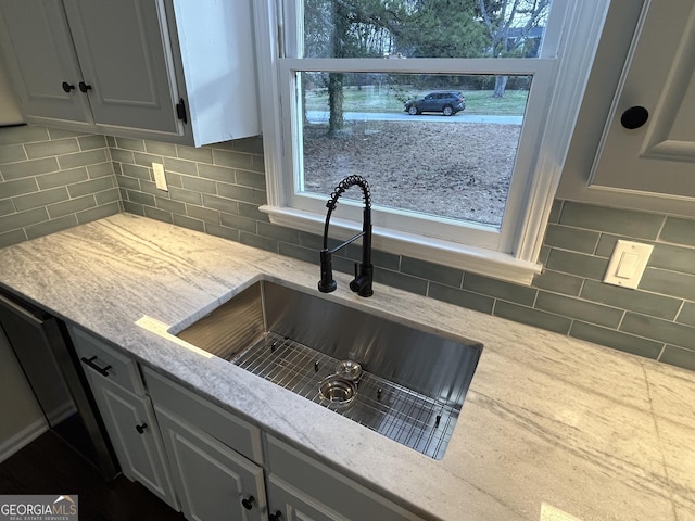 kitchen featuring light stone counters, a sink, backsplash, and dishwashing machine