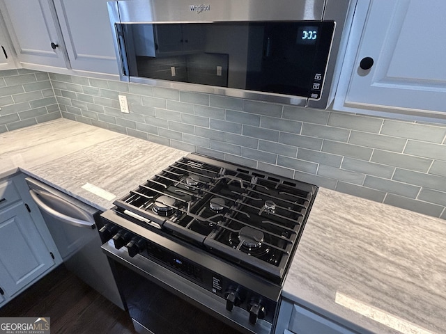 kitchen with light countertops, stainless steel microwave, backsplash, gas stove, and white cabinetry