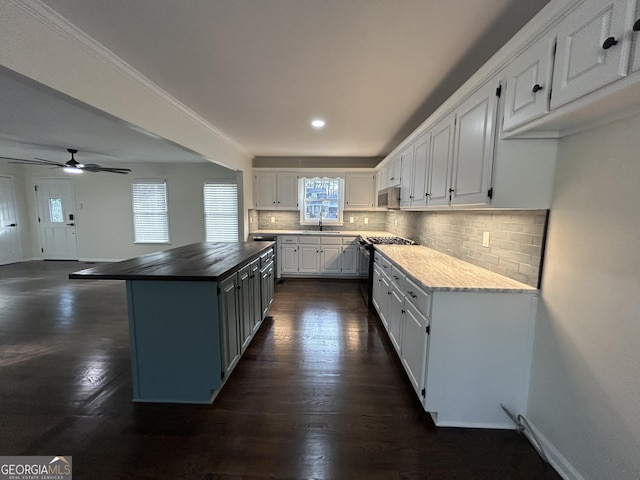 kitchen with decorative backsplash, white cabinets, a kitchen island, appliances with stainless steel finishes, and wooden counters