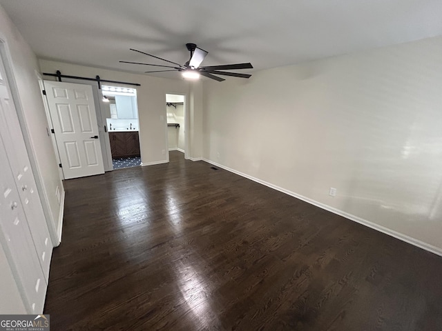 interior space with baseboards, a barn door, a ceiling fan, and dark wood-type flooring