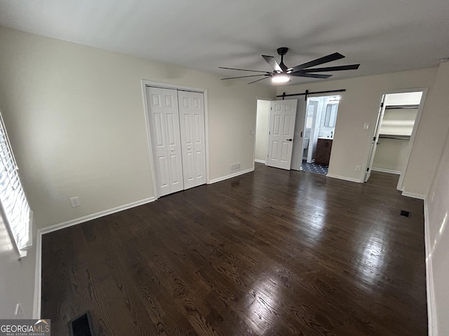 unfurnished bedroom featuring a barn door, dark wood-style flooring, visible vents, baseboards, and a closet