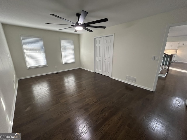 unfurnished bedroom featuring ceiling fan, dark wood-style flooring, visible vents, baseboards, and a closet