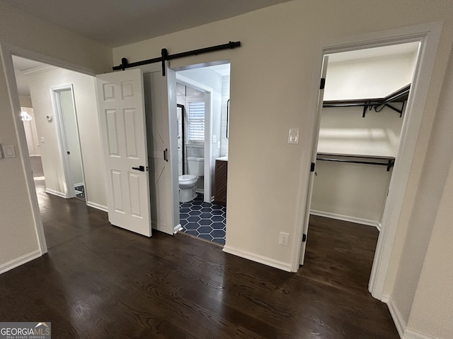 unfurnished bedroom featuring connected bathroom, a barn door, a spacious closet, and dark wood-style flooring