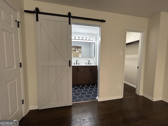 unfurnished bedroom with ensuite bath, a barn door, dark wood-style flooring, and a sink